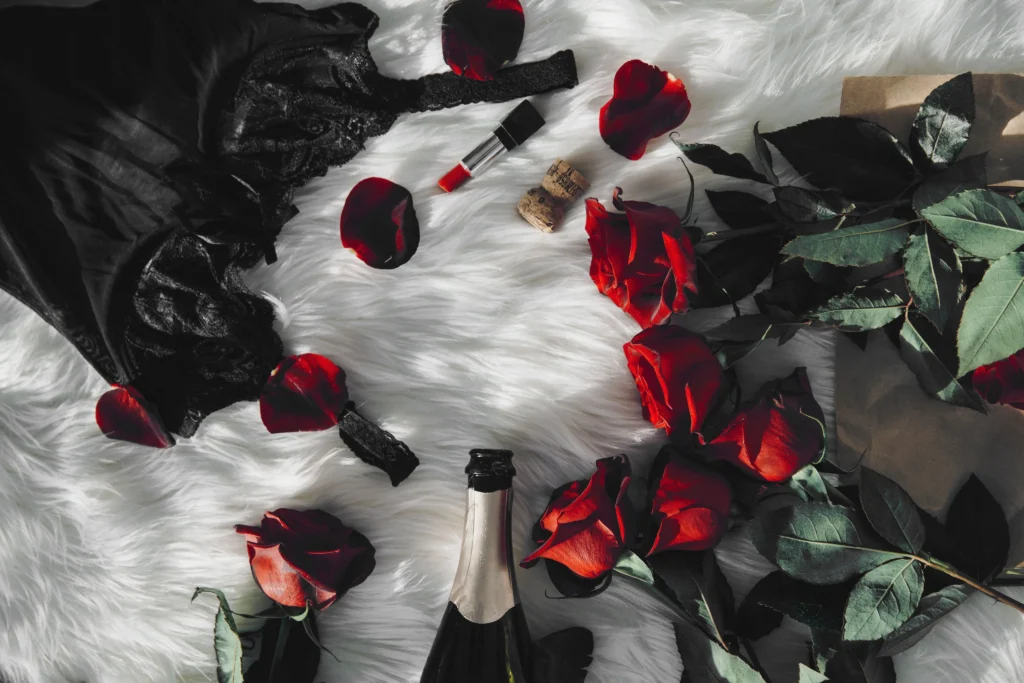Lingerie noire en dentelle, roses rouges et champagne sur fourrure blanche